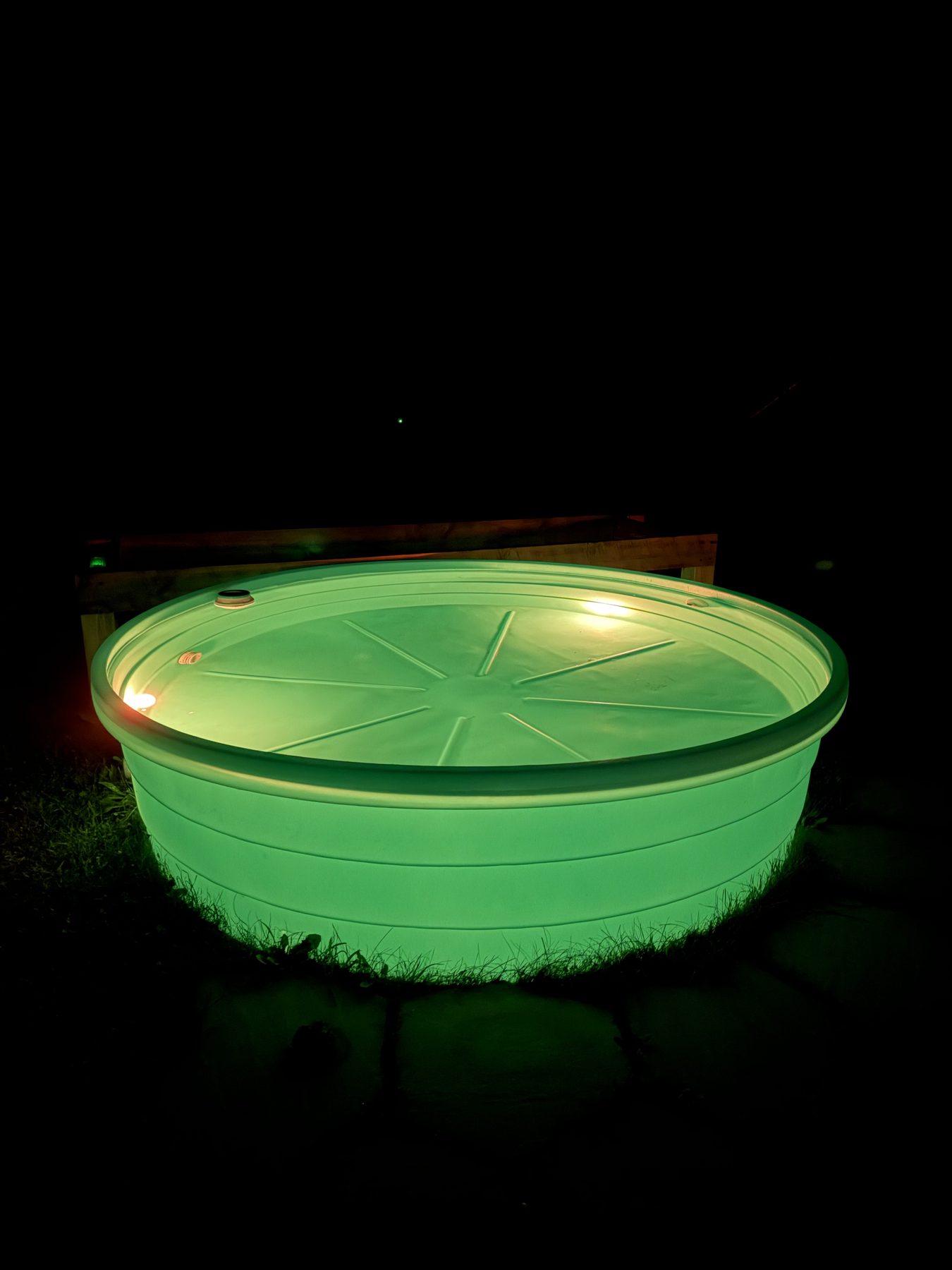 Stock tank pool glowing green at night from magnetic underwater pool lights