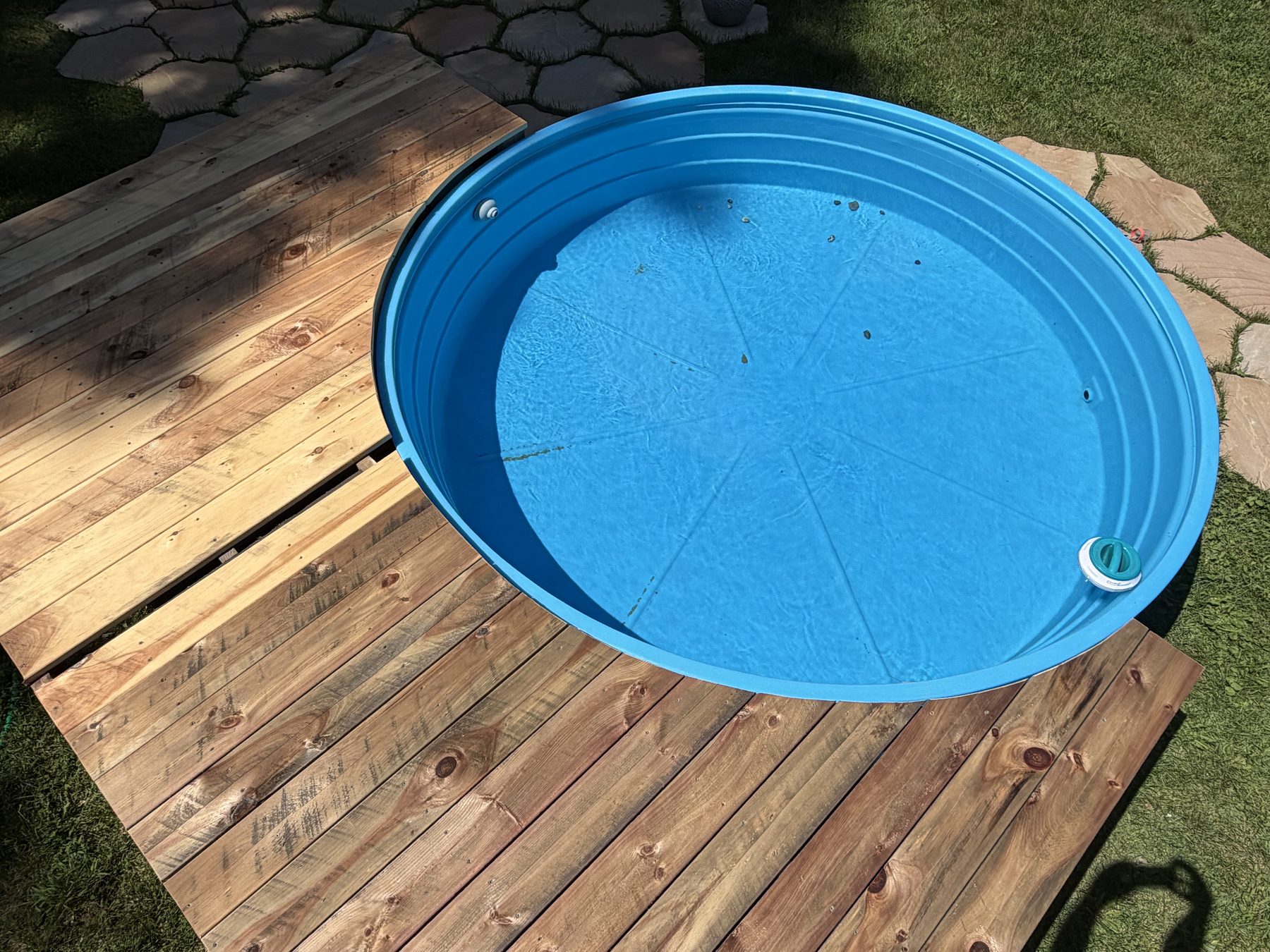 Aerial view of a round stock tank pool set into a wood deck and stone patio