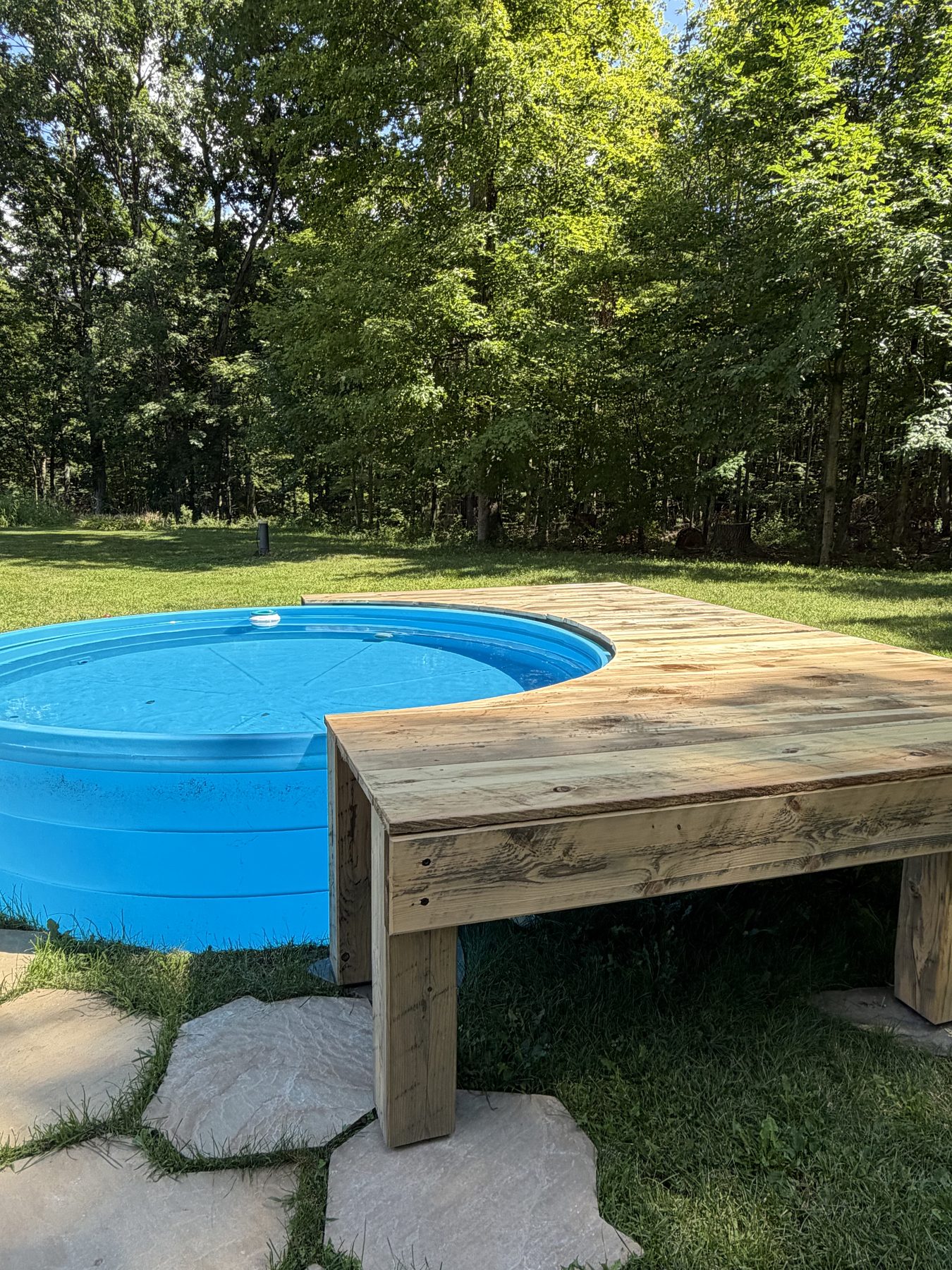Curved wood deck wrapping around a stock tank pool with forest in the background